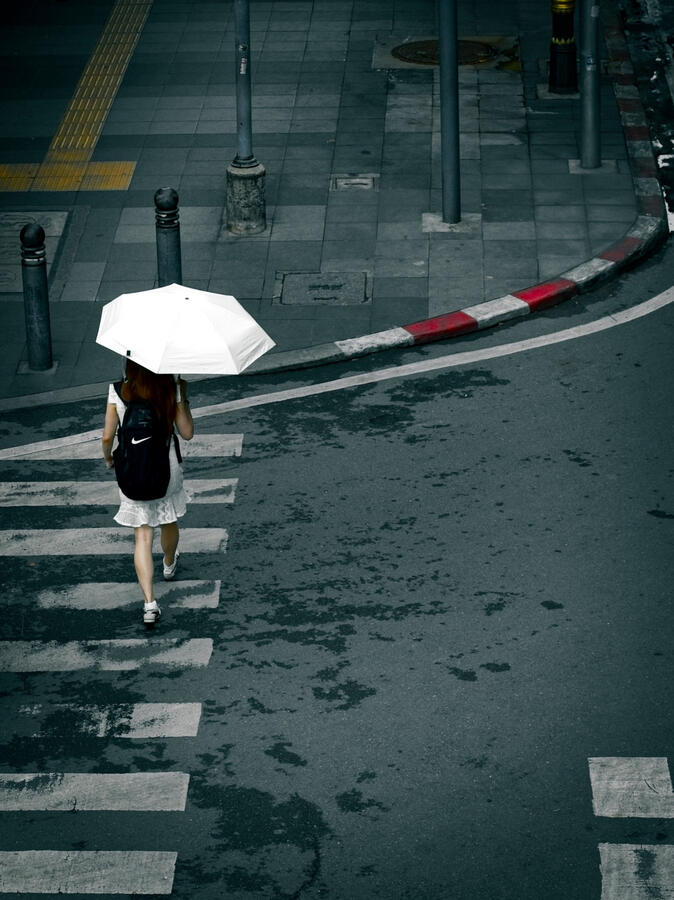 Bangkok, Thailand Woman carrying a white umbrella across a wet street in Bangkok, Thailand.